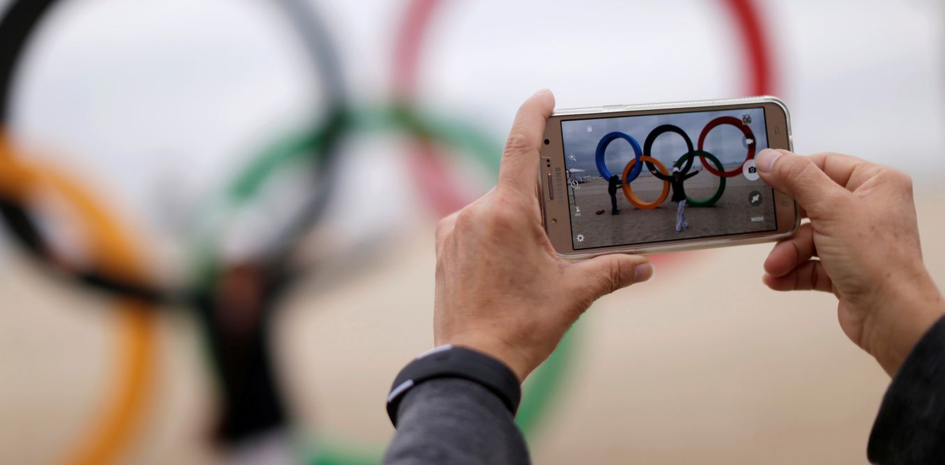 A_woman_takes_pictures_with_a_mobile_phone_in_front_of_the_Olympic_rings_placed_at_the_Copacabana_beach_ahead_of_the_2016_Rio_Ol.jpeg